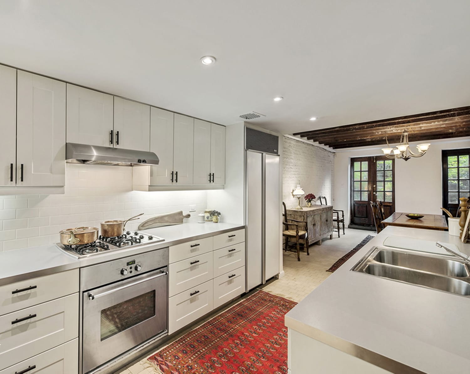 Modern kitchen with white cabinets, stainless steel appliances, and warm lighting, connected to a dining area with rustic decor.