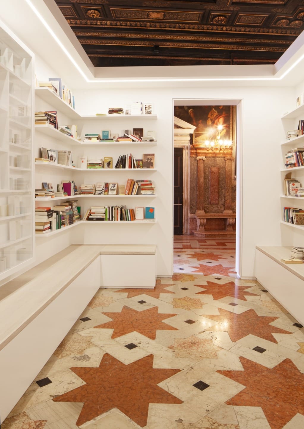 Modern library room with white shelves, wooden bench seating, and a decorative star-patterned marble floor.