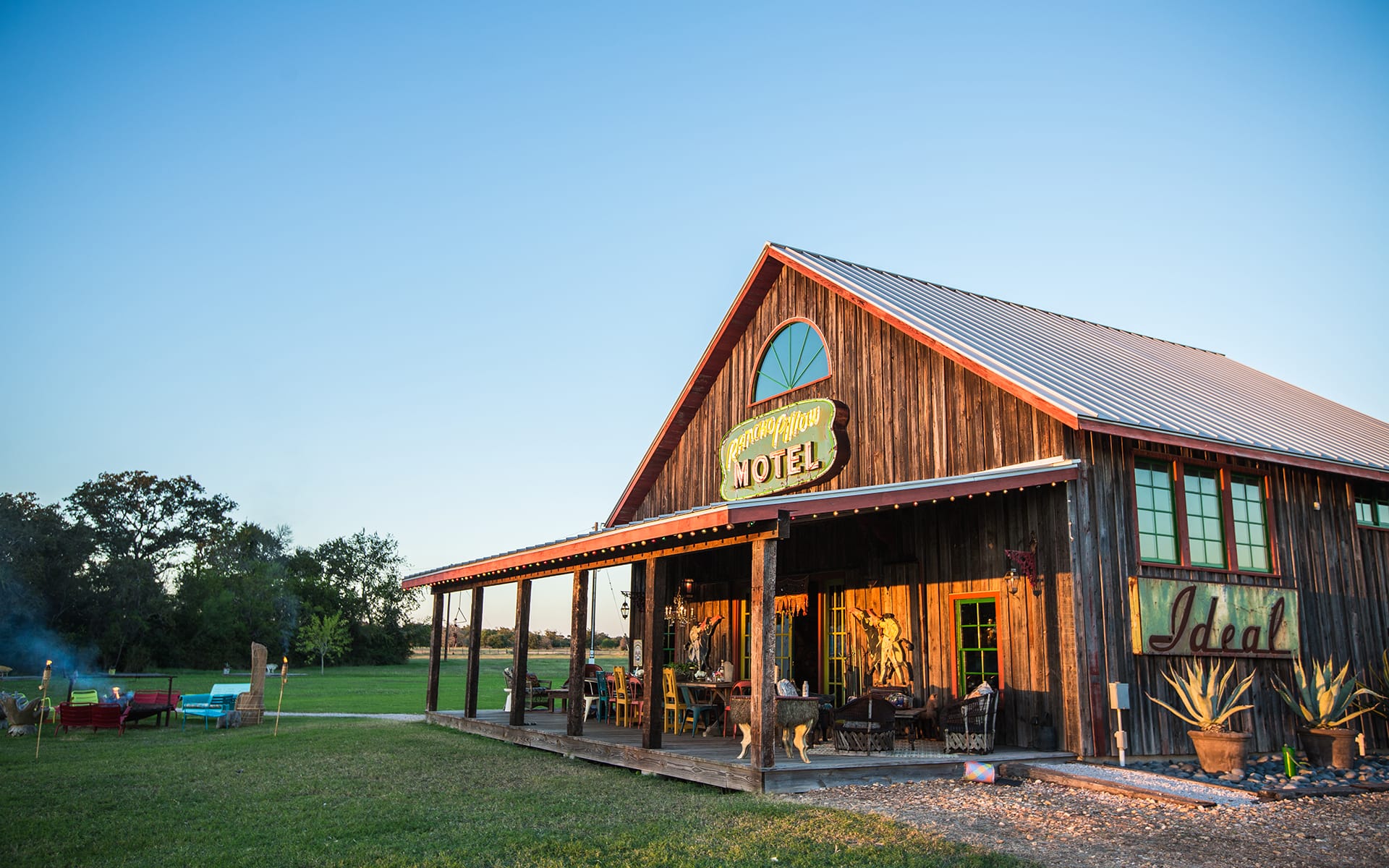 Rustic wooden motel building with a porch, surrounded by trees and a clear blue sky in the background.
