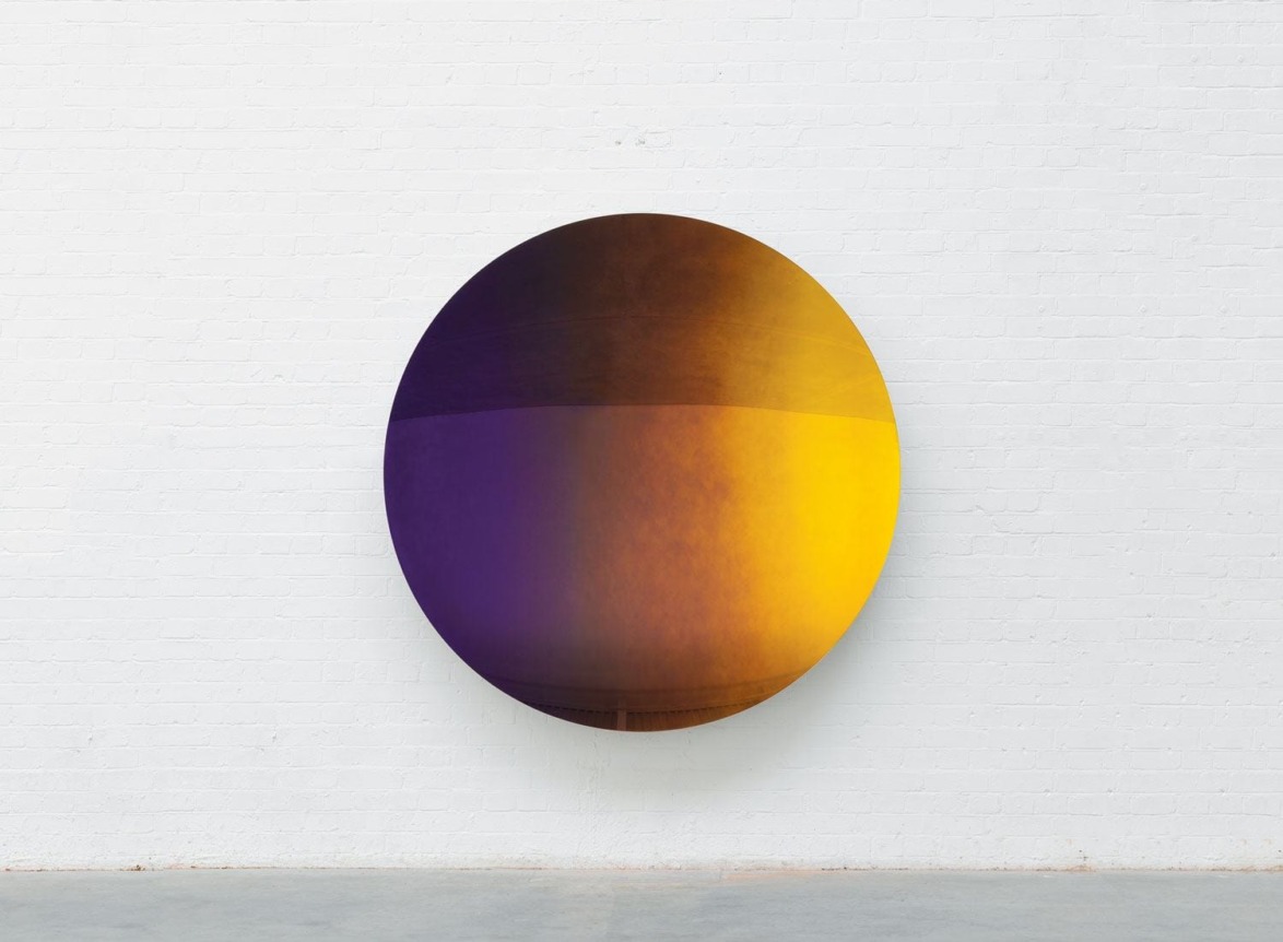 Large round wall art with a gradient blend of purple and yellow on a white brick wall background.