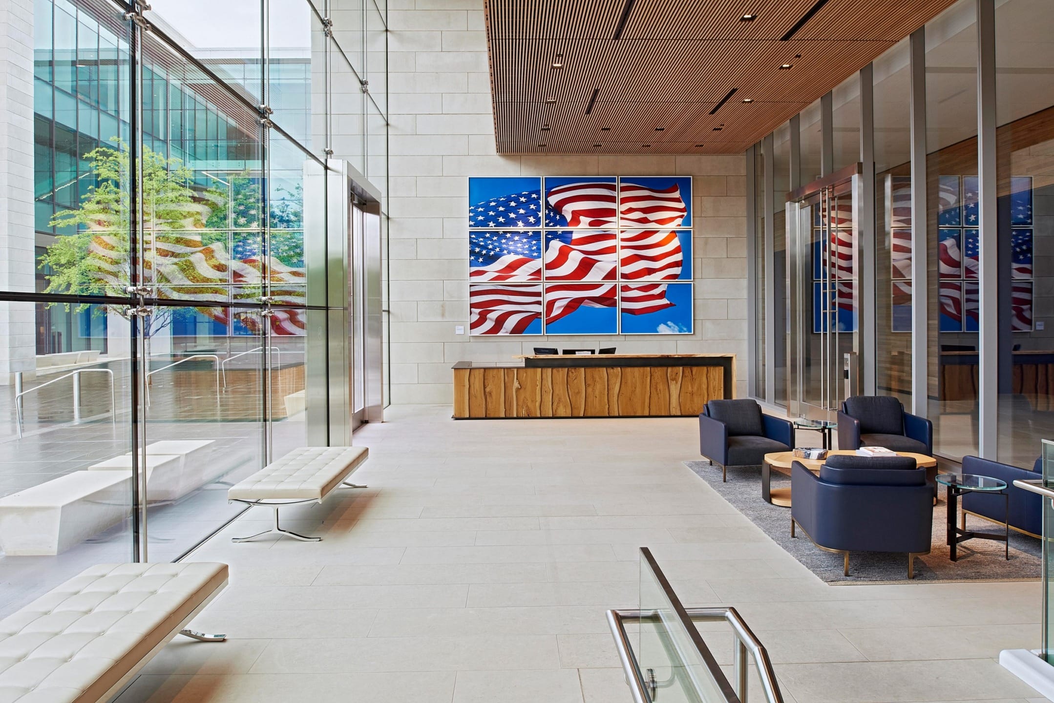 Modern office lobby with glass walls, American flag artwork, wooden reception desk, and stylish seating area.