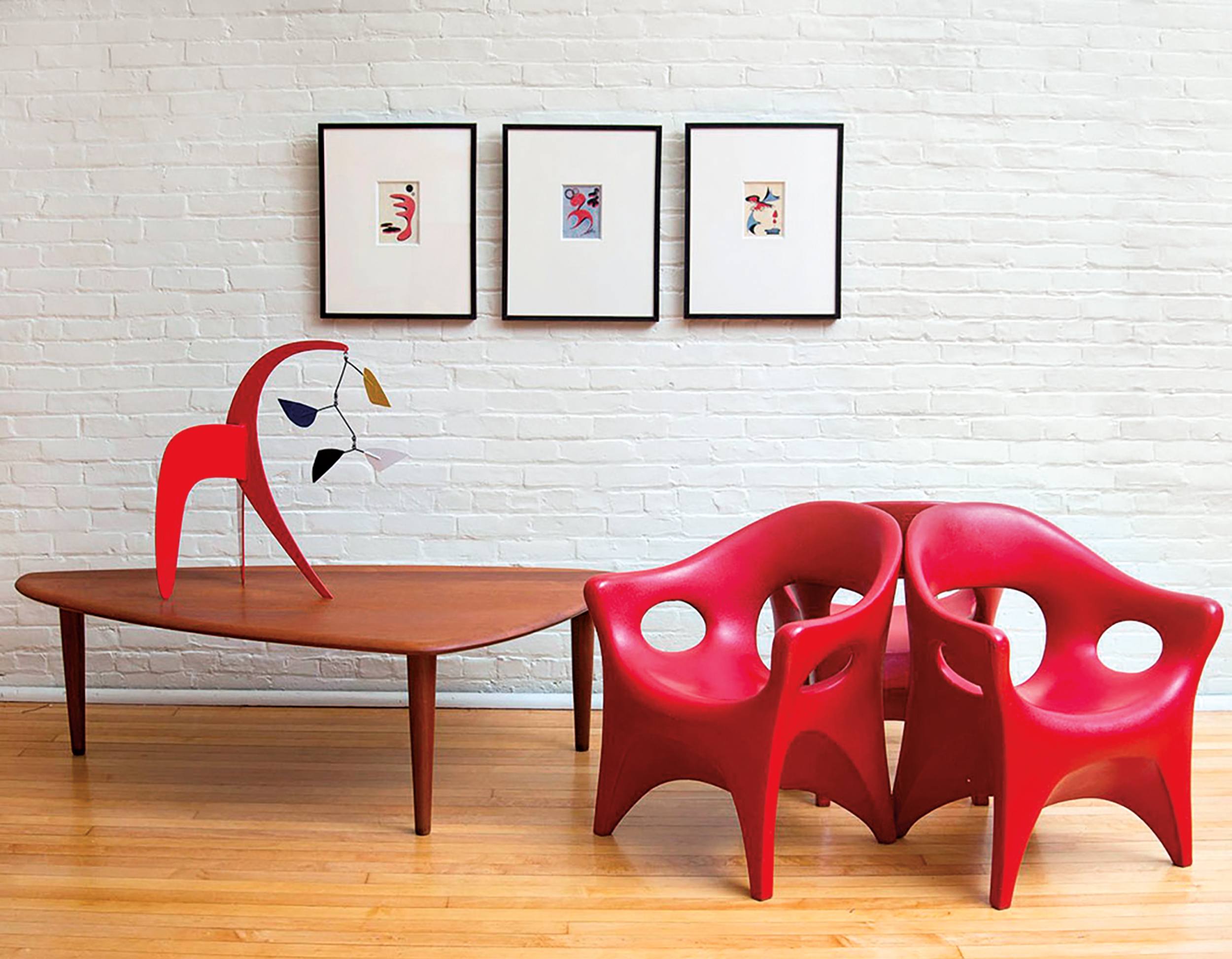 Modern living room with red chairs, wooden coffee table, abstract art on a white brick wall, and wooden floor.