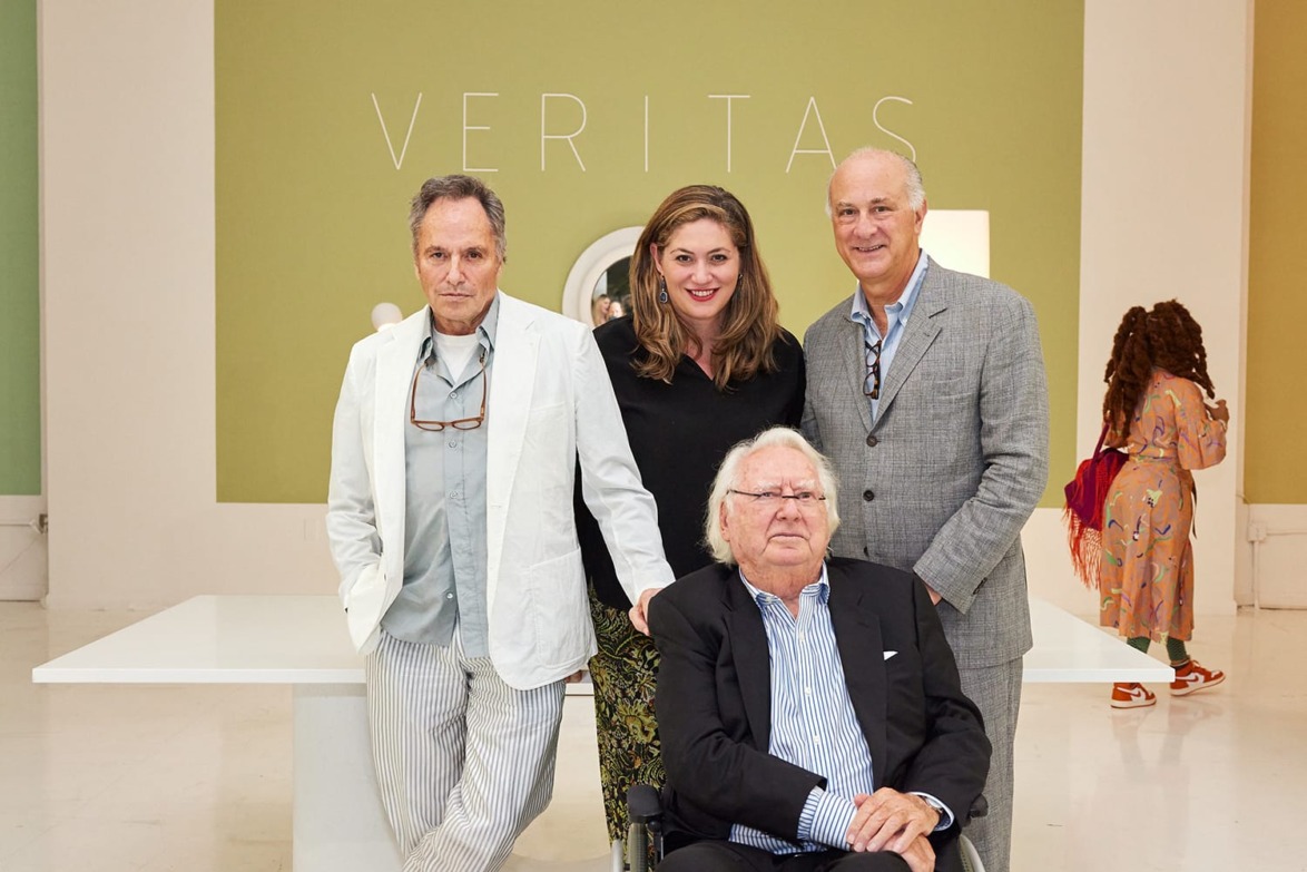 Four people posing together in an art gallery with the word Veritas on the wall in the background.