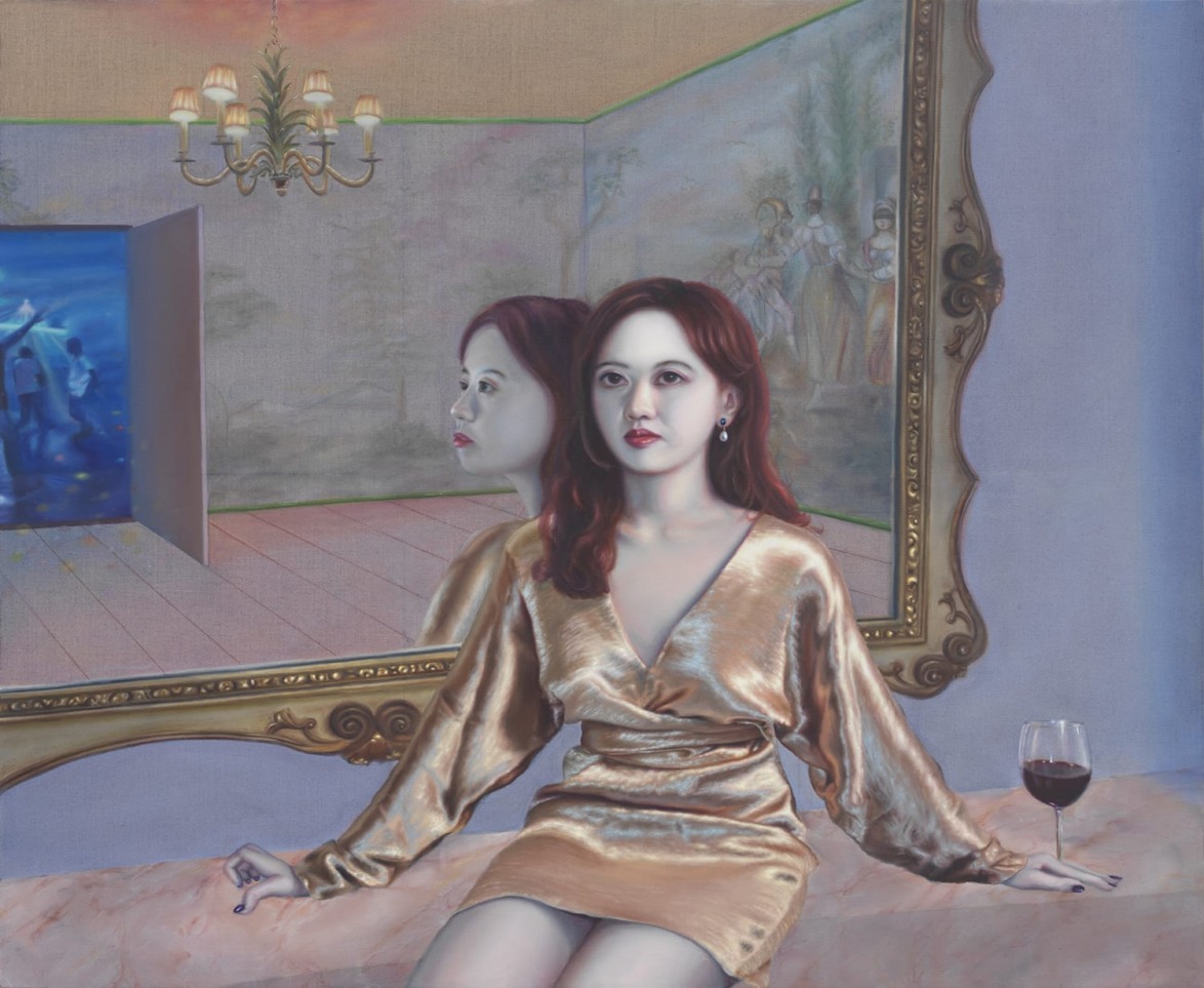 Woman in a golden dress sits by a mirror with her reflection, near a glass of red wine, chandelier and paintings in the background.