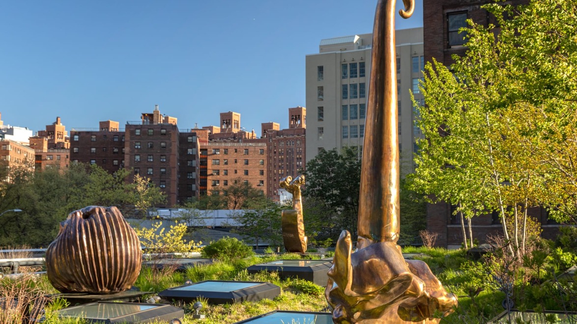 Bronze sculptures on a rooftop garden with urban buildings in the background under a clear blue sky.