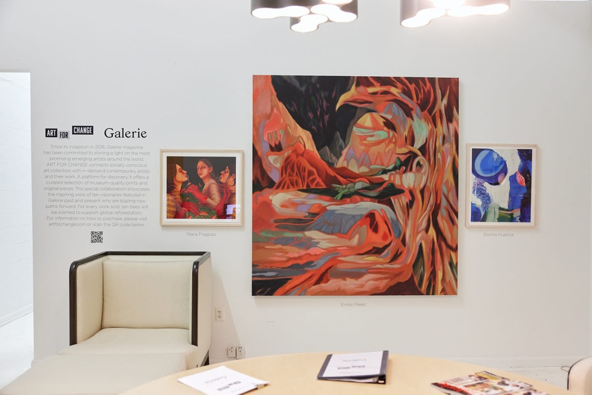 Art gallery wall displaying three colorful paintings with abstract and figurative elements next to a modern chair.