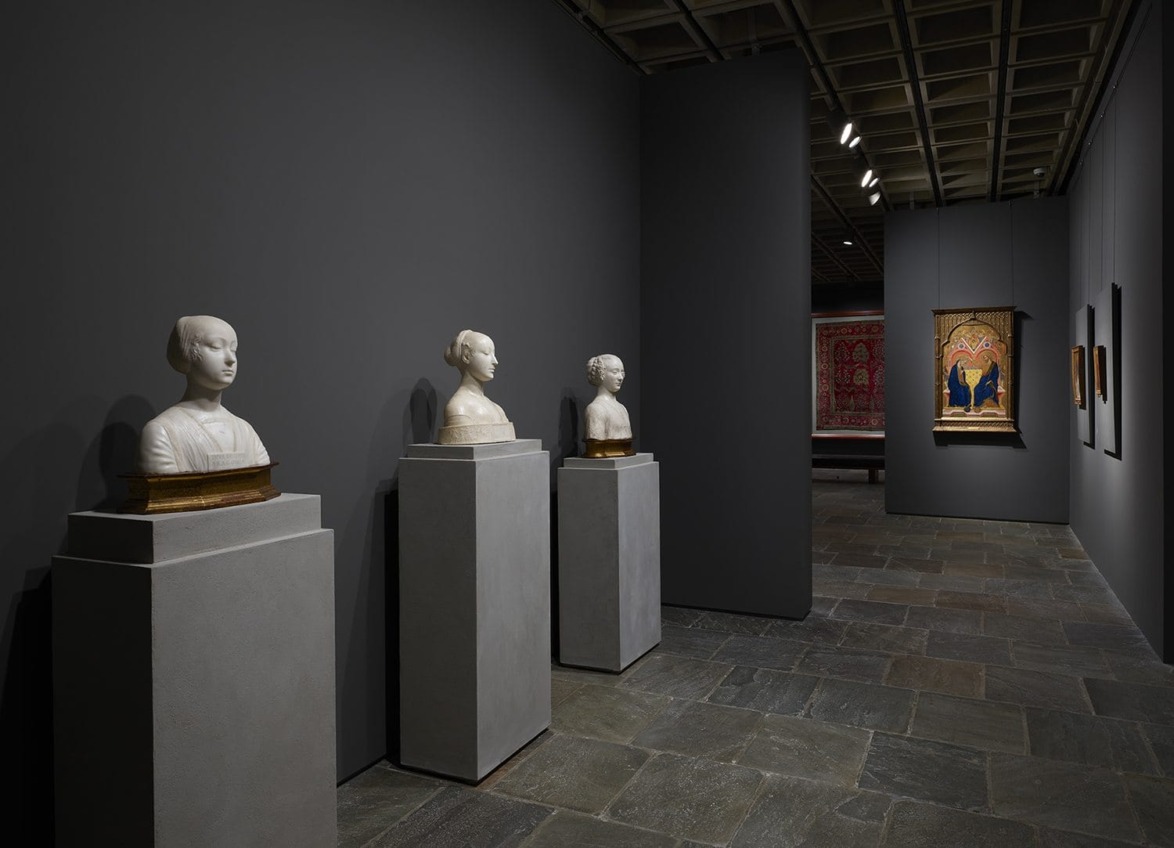 Art gallery interior with classical busts on pedestals and framed paintings on dark walls.