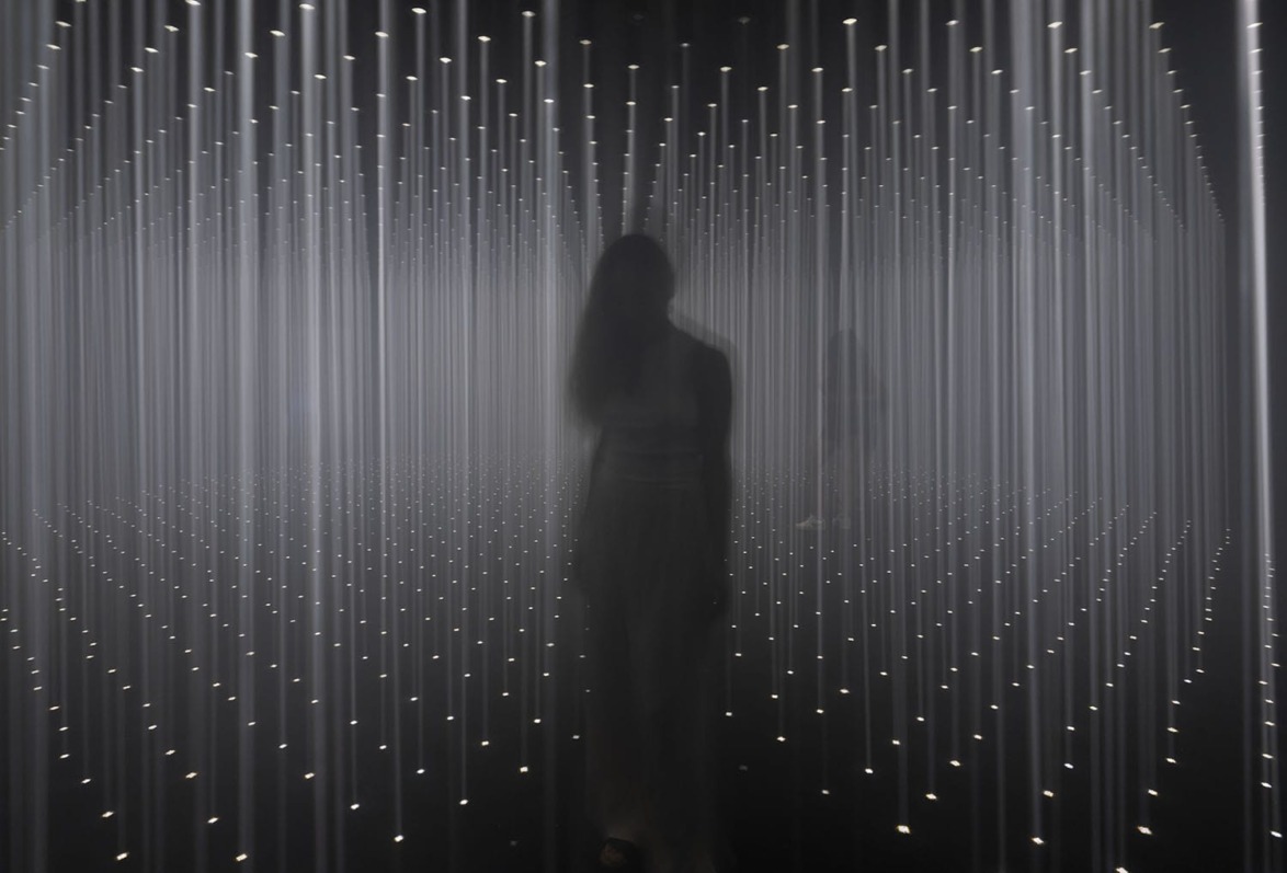 Silhouetted person standing in an illuminated room with vertical light beams creating a futuristic atmosphere.