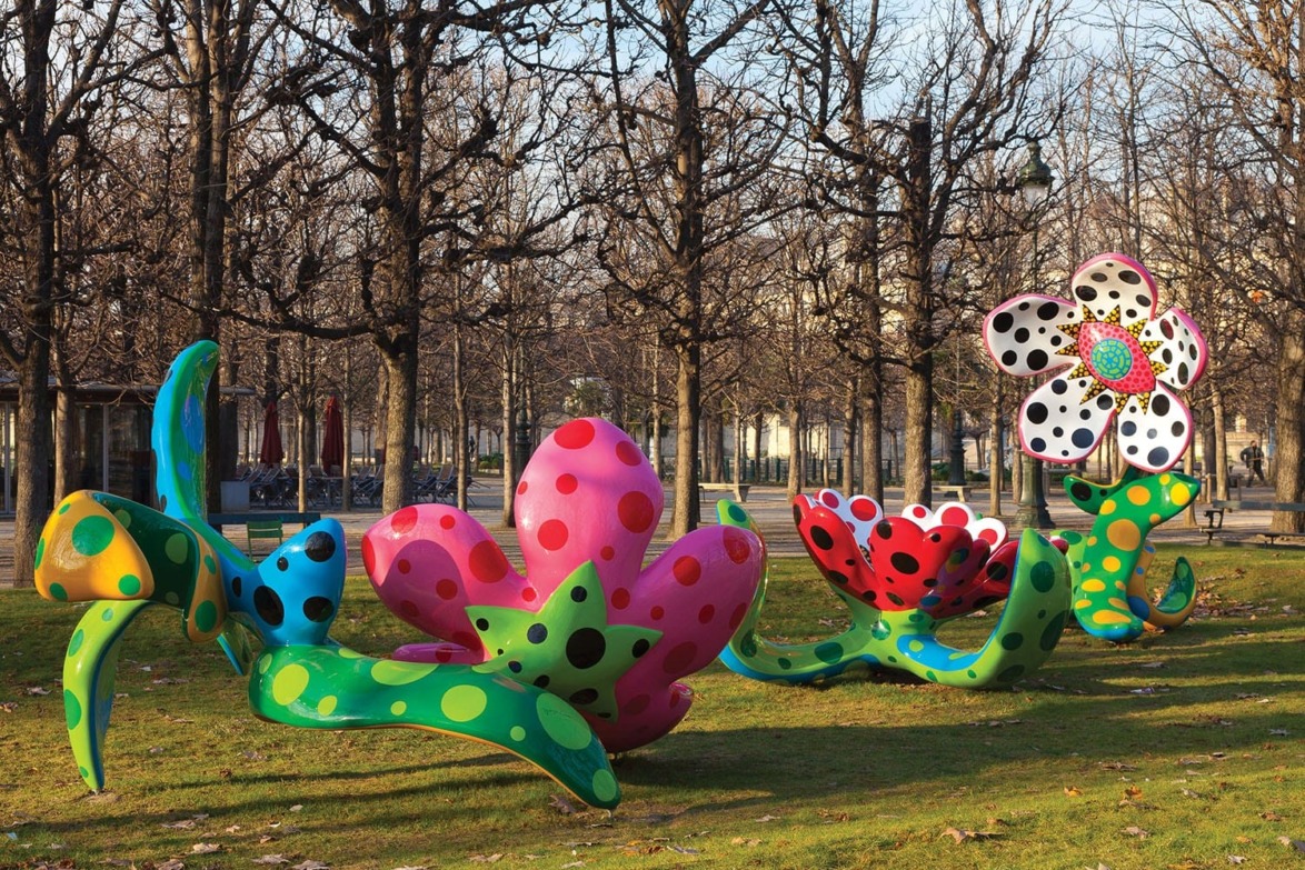 Colorful polka-dotted flower sculptures in a park with bare trees and green grass.