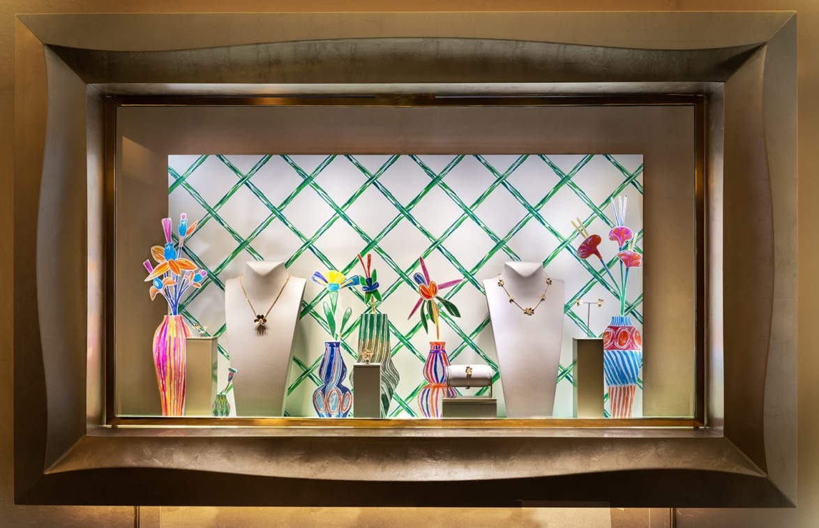Colorful jewelry store window display with mannequins and vibrant abstract flowers in vases on a geometric background.