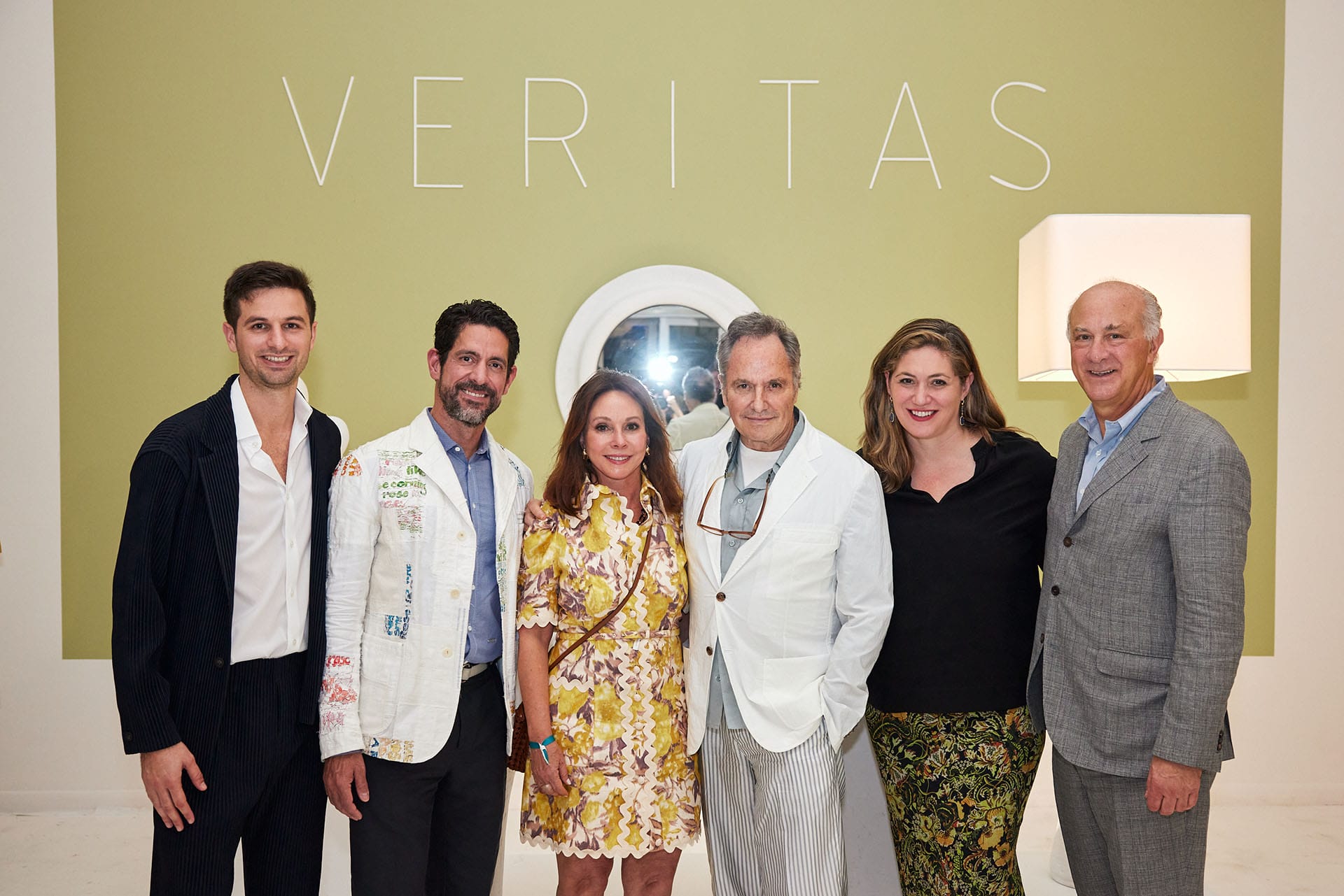 Group of six people posing in front of a green wall with the word "VERITAS" displayed above.