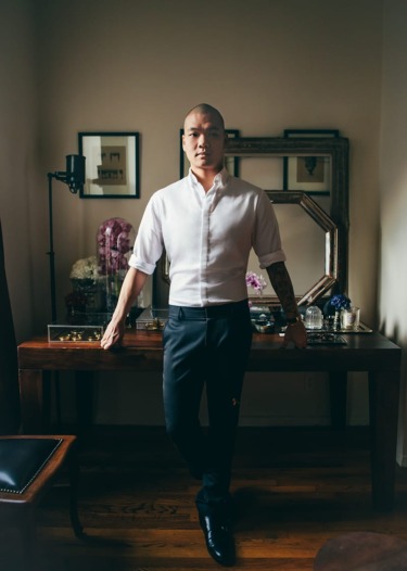 Person in a white shirt and dark pants standing in a stylish room with a wooden table and decorative mirrors.