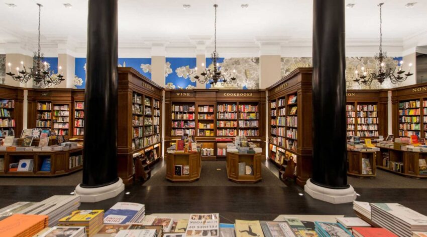 Interior of a bookstore with tall columns, chandeliers, and shelves filled with books on various topics.