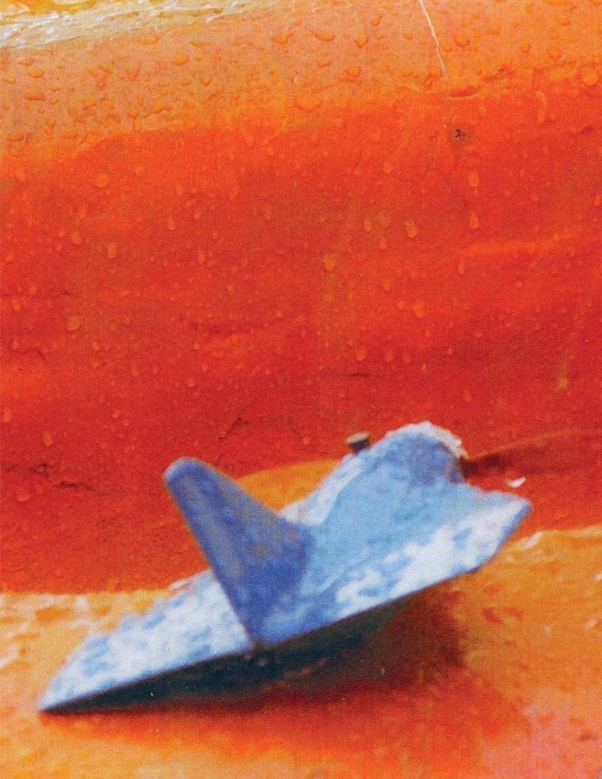 Blue paper airplane on a vibrant orange surface with water droplets