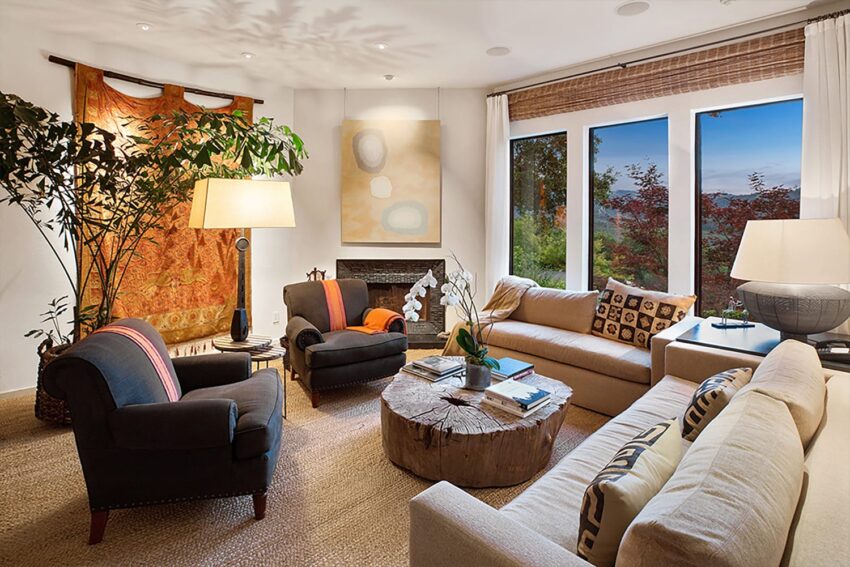 Cozy living room with sofas, armchairs, large tree, lamps, and a window with a scenic view.