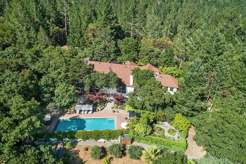 Aerial view of a large house with a pool surrounded by dense green forest.