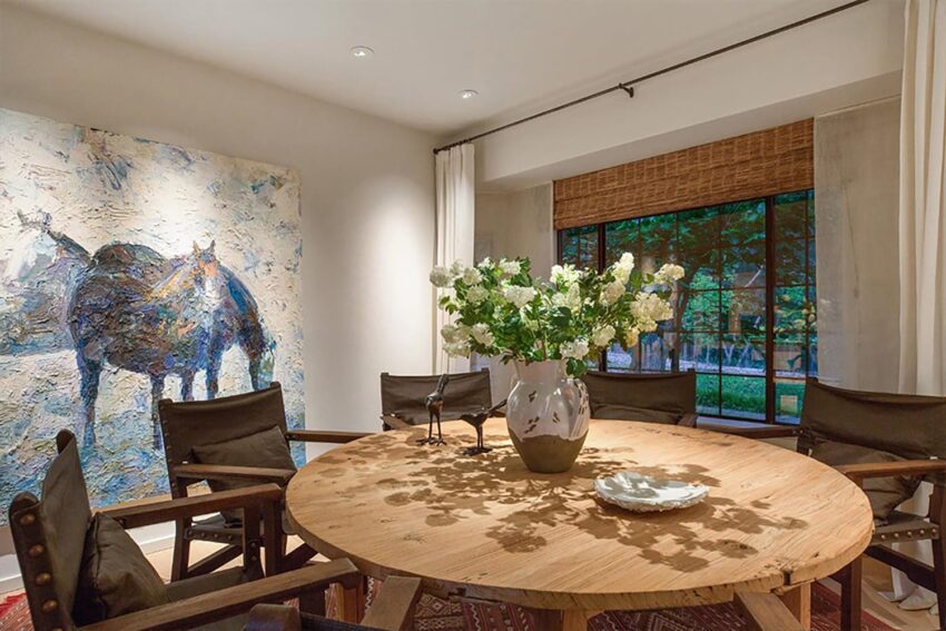 Modern dining room with round wooden table, black chairs, decorative vase of flowers, and a large abstract horse painting.