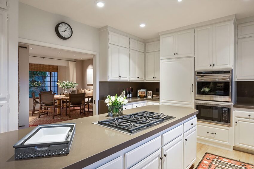 Modern kitchen with white cabinets, black countertops, and a stove on the island, opening to a dining area.