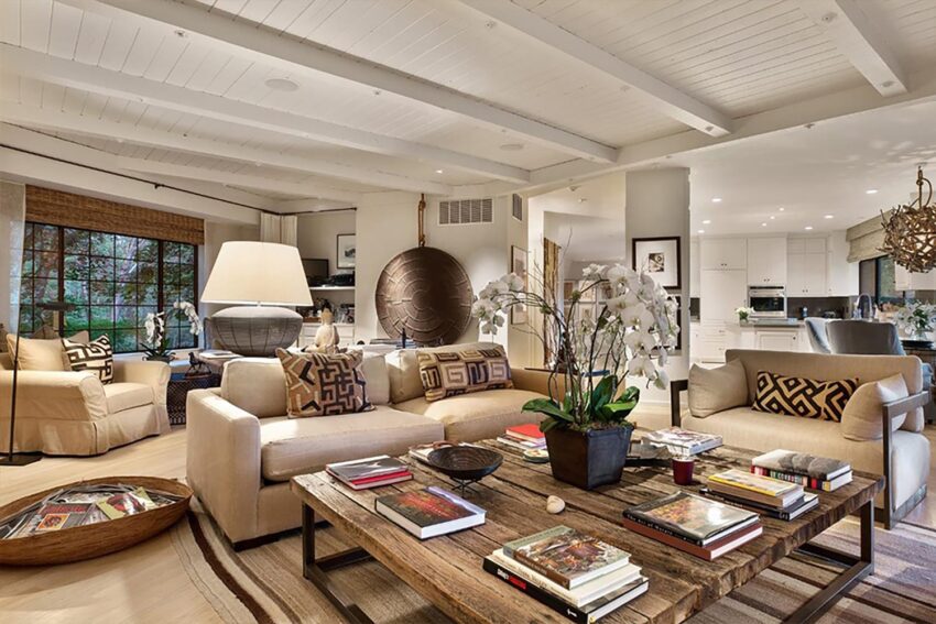 Spacious living room with cozy beige sofas, wooden coffee table, books, large lampshade, and open kitchen in the background.