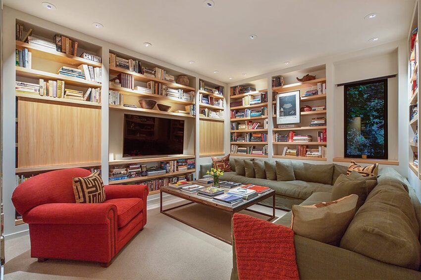 Cozy living room with bookshelves, a large TV, red armchair, and L-shaped sofa centered around a coffee table.