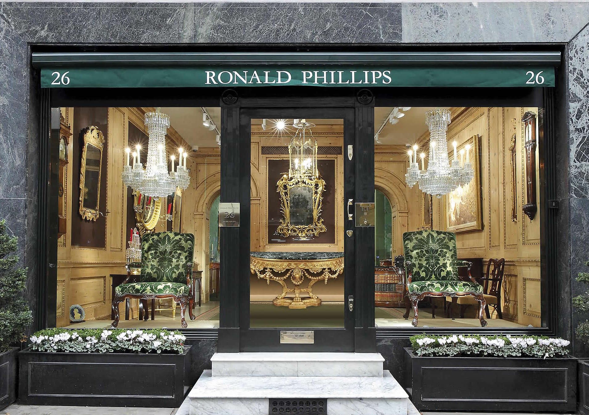 Antique furniture store with elegant chairs, table, and chandelier visible through a large glass window.