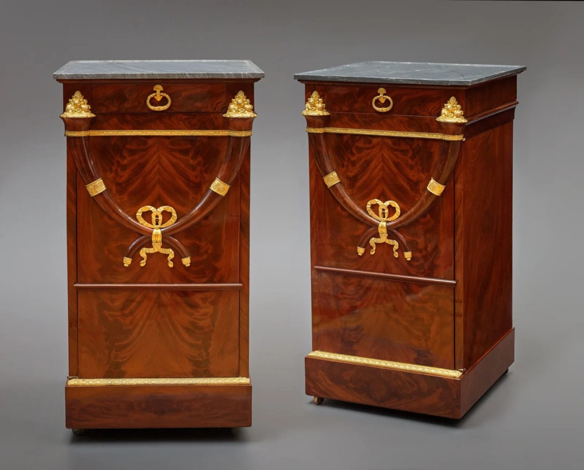 Pair of elegant wooden pedestals with intricate gold detailing and black marble tops, set against a plain background.