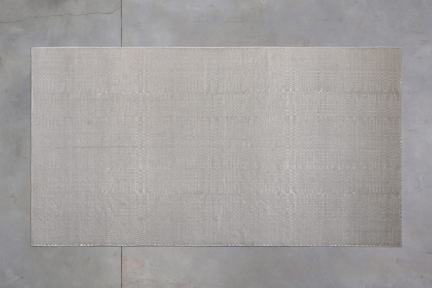 Rectangular beige rug with subtle texture placed on a concrete floor background.