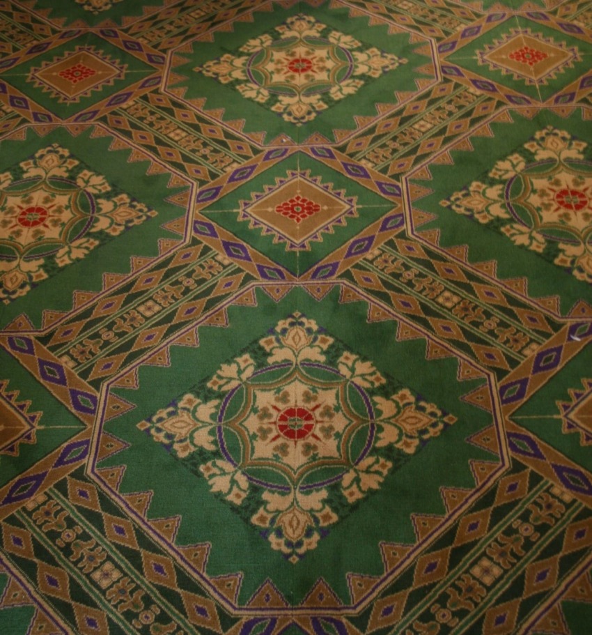 Intricate green and gold patterned carpet design with geometric and floral motifs.