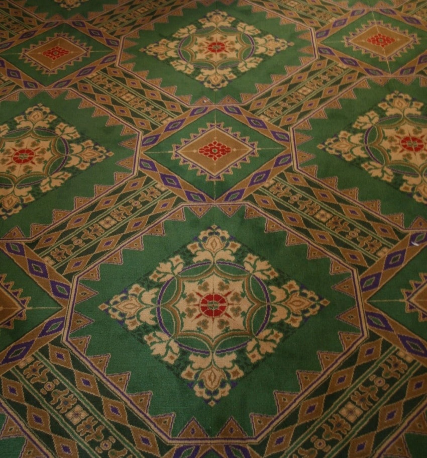 Intricate green and gold patterned carpet design with geometric and floral motifs.