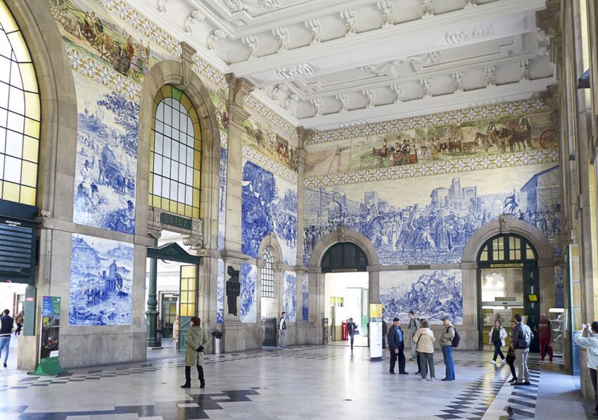 Interior of São Bento Railway Station in Porto with blue and white tile murals and people walking around