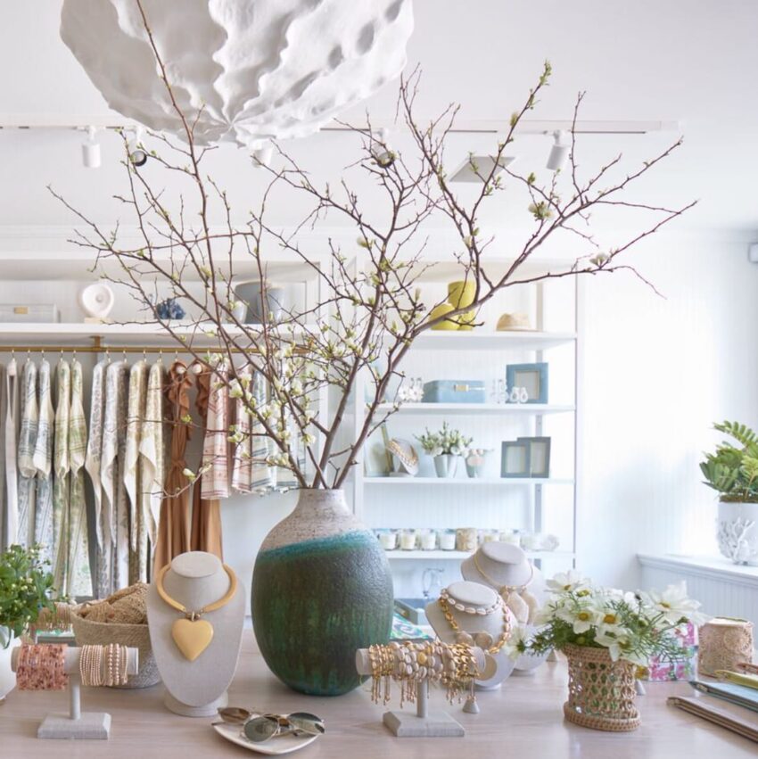 Chic boutique display with branches in vase, jewelry, and decor items on a white table.