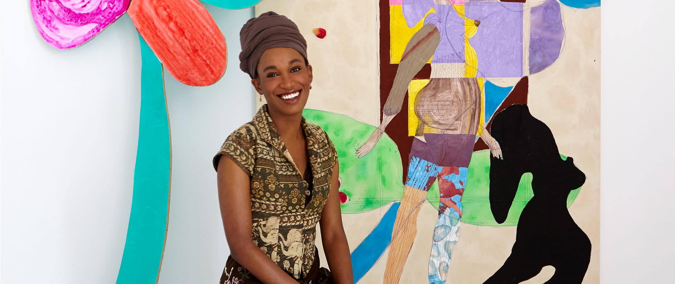Smiling woman in patterned dress and headwrap standing beside colorful abstract painting.