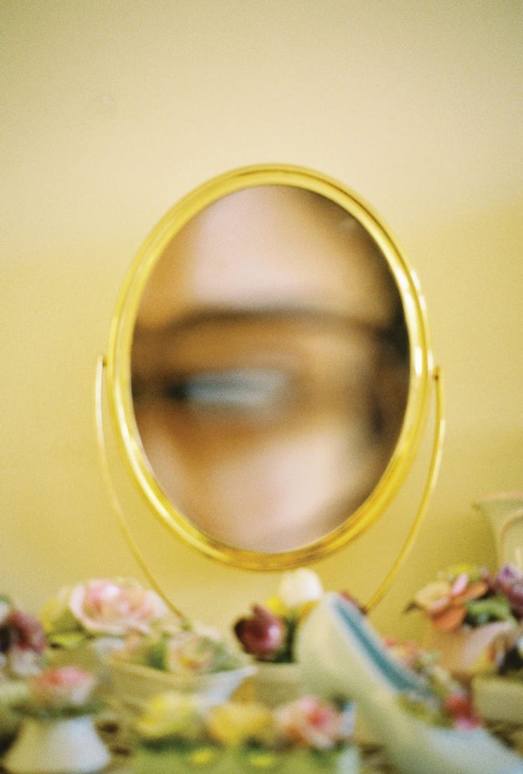 Blurred reflection of an eye in a small oval-shaped mirror surrounded by colorful artificial flowers.