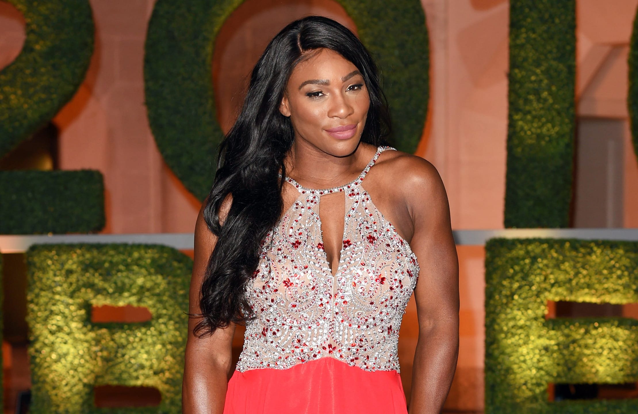 Tennis player at a formal event wearing a beaded gown with a green backdrop.