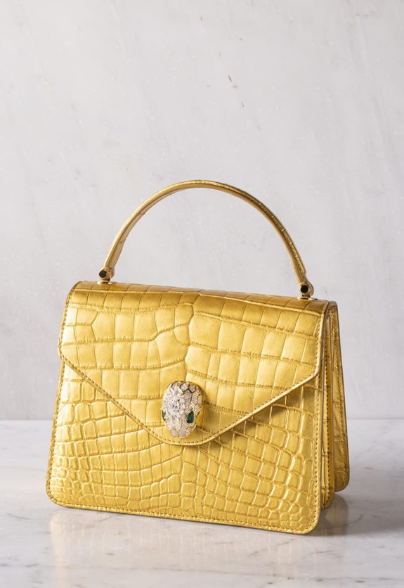 Elegant gold handbag with reptile texture and an ornate clasp, resting on a marble surface.