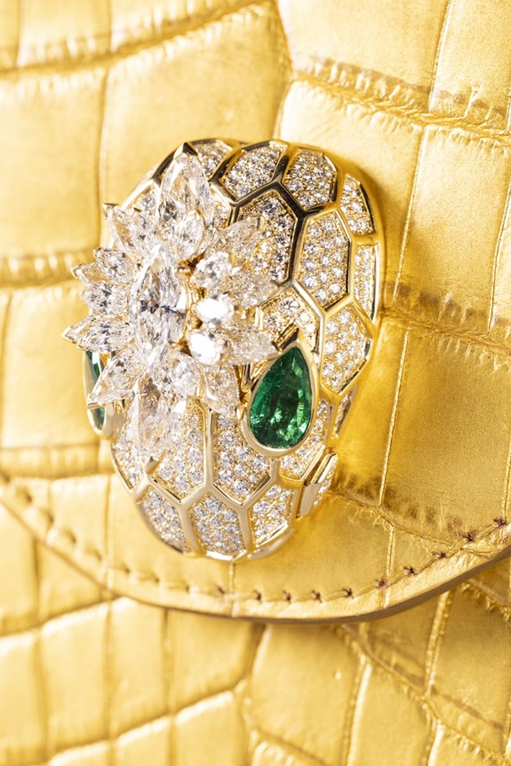 Gold handbag with a diamond and emerald-encrusted snakehead clasp, featuring hexagonal patterns and sparkling gemstones.