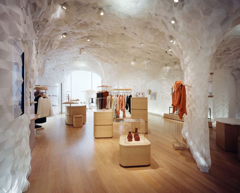 Fashion boutique interior with unique white textured walls, wooden flooring, and modern clothing displays.