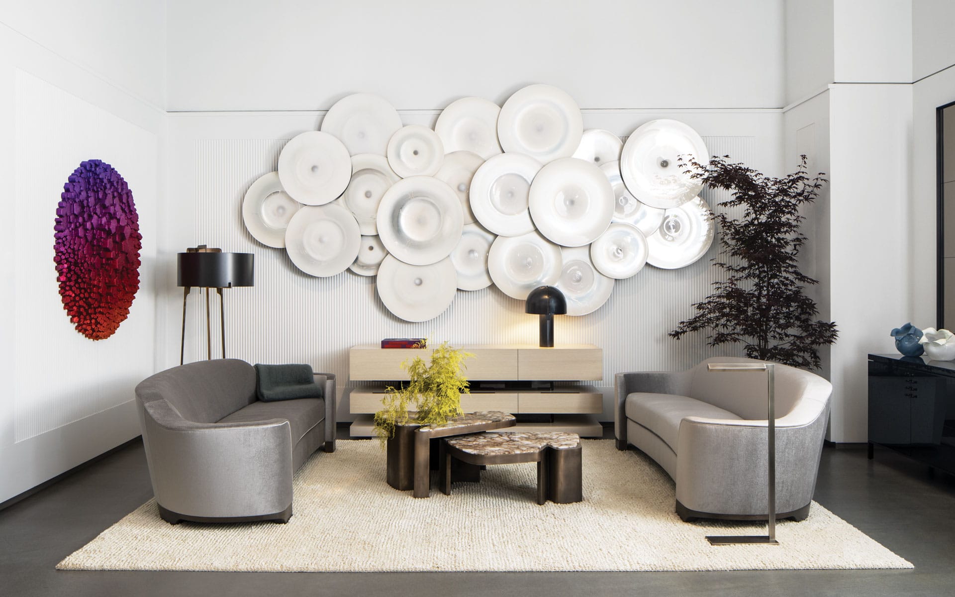 Modern living room with gray sofas, artistic wall decor, round coffee tables, and a floor lamp on a light rug.