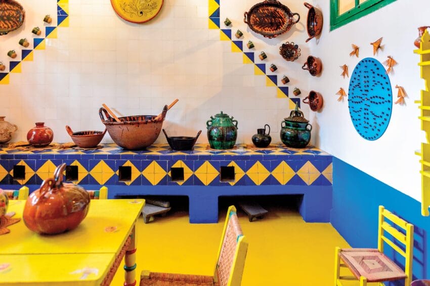 Colorful kitchen with vibrant pottery and unique wall decorations, featuring blue and yellow geometric patterns.
