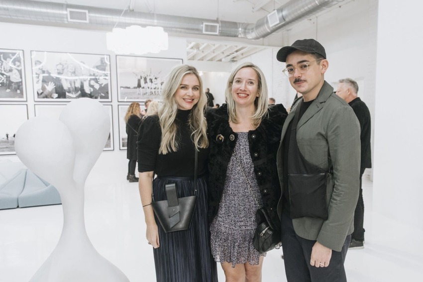 Three people posing together in a modern art gallery with monochrome artwork on the walls.