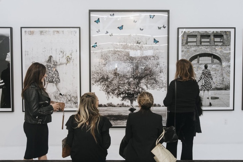 People observing black and white photographs in an art gallery, with butterflies on one artwork.
