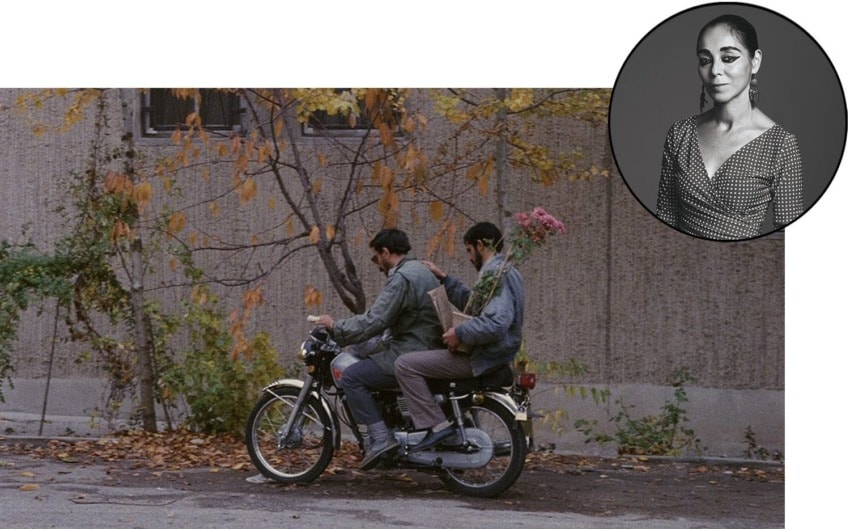Two people on a motorcycle with flowers, against a backdrop of a concrete wall and autumn trees.