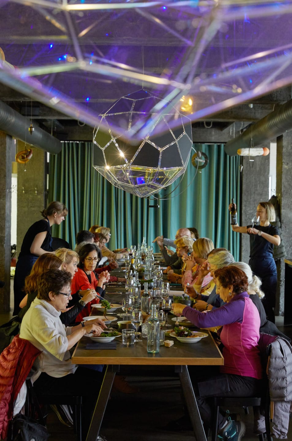 Group of people enjoying a meal together in a modern restaurant setting with decorative lighting overhead