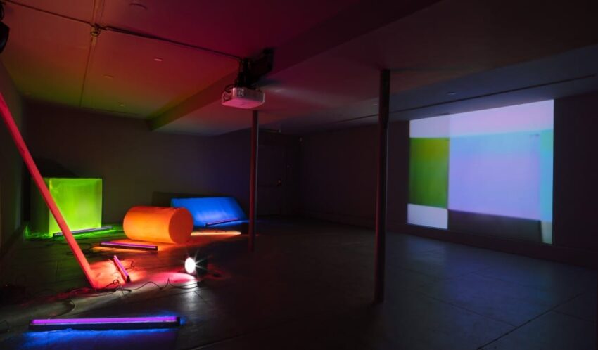 Dimly lit room with colorful neon lights and abstract projections on the wall.