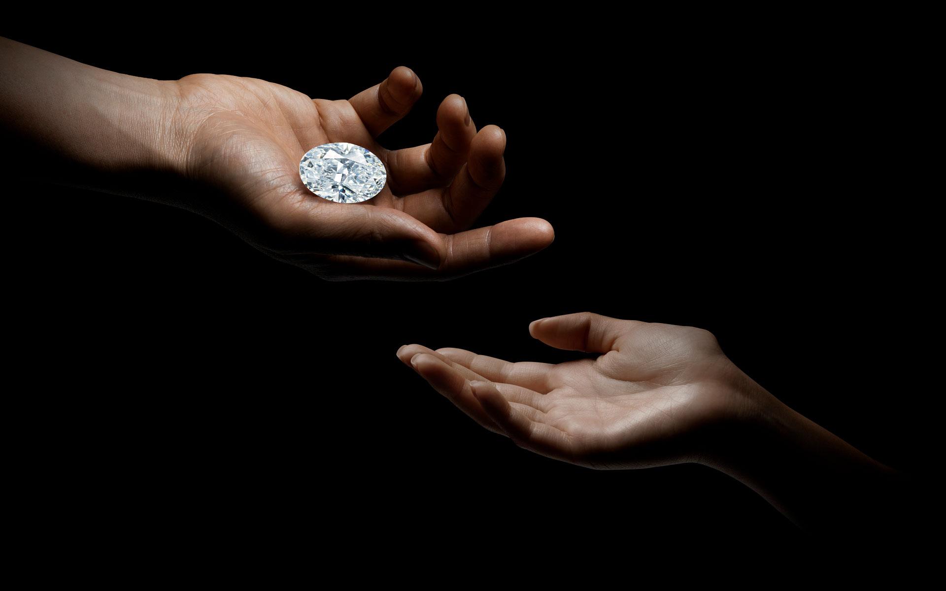 Hands exchanging a large diamond on a black background.