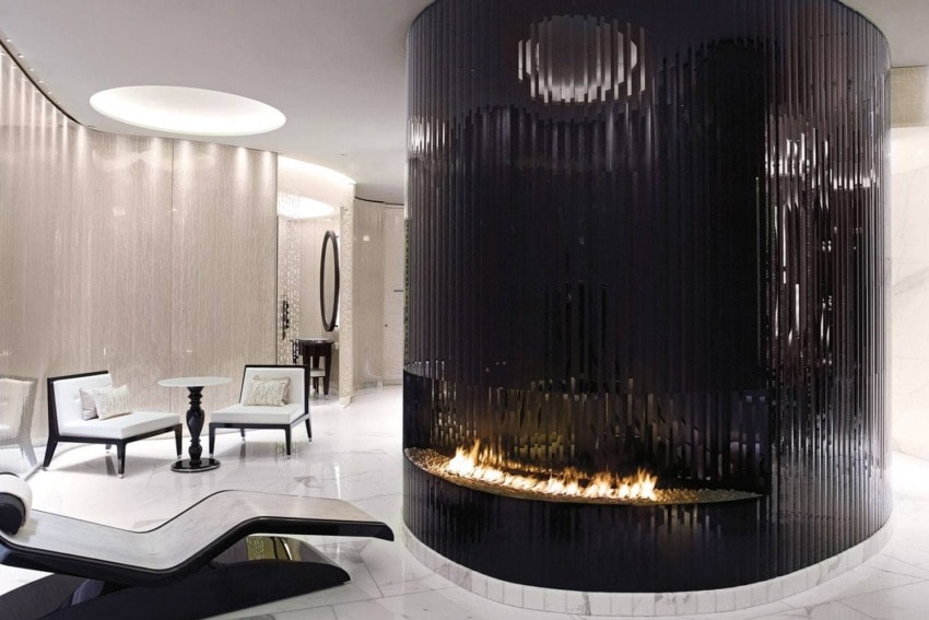 Modern lounge with sleek black circular fireplace, white marble floor, and contemporary seating.