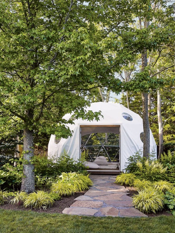 Dome-shaped structure surrounded by lush green trees and plants with a stone pathway leading to the entrance.