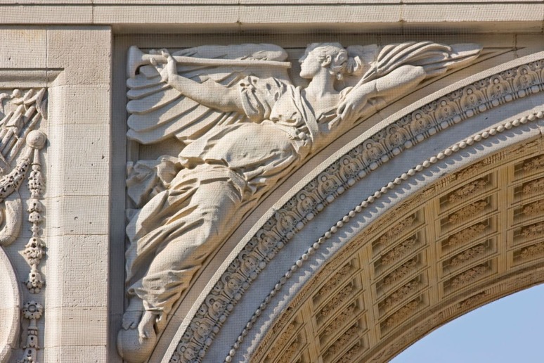 Stone relief sculpture of a winged figure with a trumpet on an arch, showcasing intricate architectural details