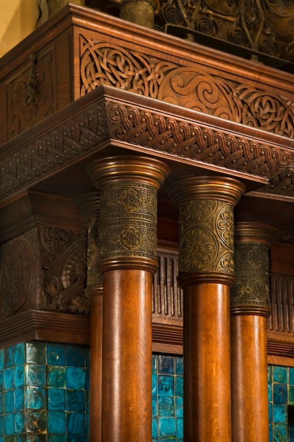 Ornate wooden pillar with intricate carvings and decorative turquoise tiles in a classical architectural style.