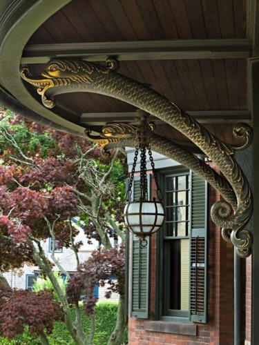 Decorative dragon-shaped corbels on a house porch with hanging lantern and trees in the background.